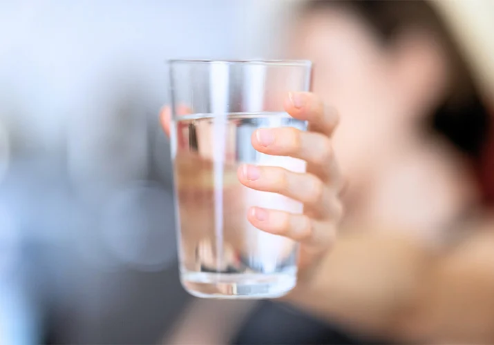 Cloudy tap water in a glass beside a Dubai bathroom tap, a sign the water tank needs cleaning.
